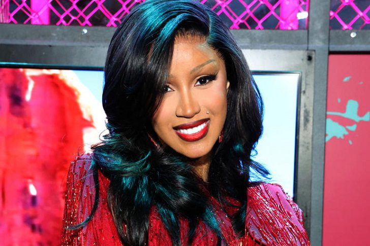 Does Cardi B write her own lyrics - Cardi B with teal-tipped wavy hair, red lipstick and dressed in a sparkling red garment.